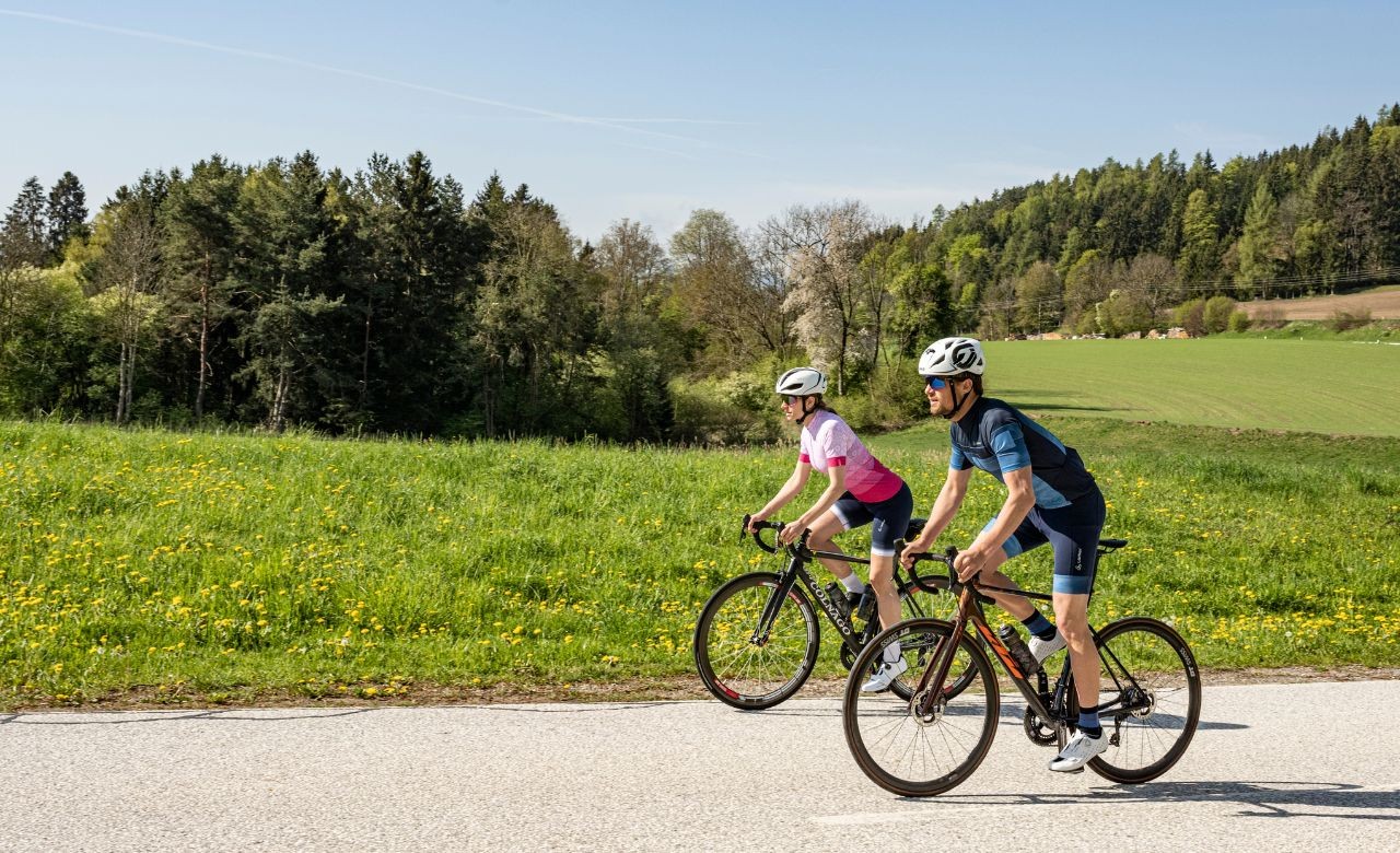 Herr in blauem Rennradtrikot und blauer Radhose gemeinsam mit Dame in Rennradtrikot in magenta und dunkelblauer Radhose.