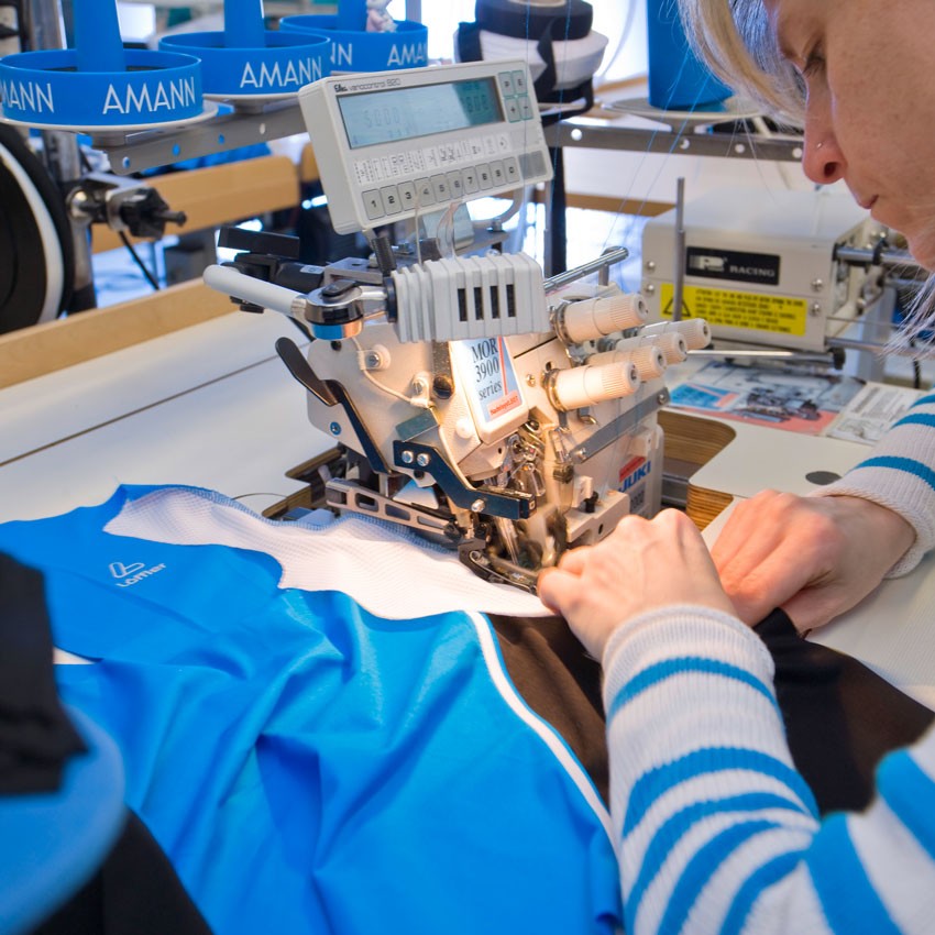 Näherin arbeitet an blauem Trikot an einer Nähmaschine.