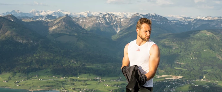 Man wearing white functional singlet, in the background mountain panorama with lake
